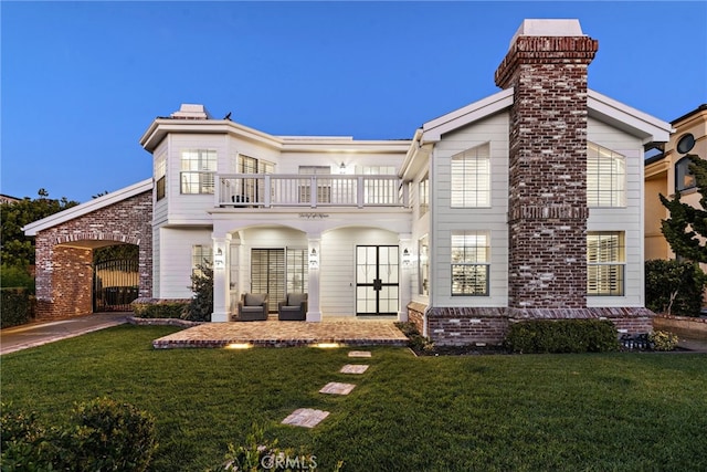 view of front of property with brick siding, a patio, a chimney, a front yard, and a balcony