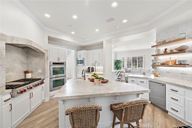 kitchen with crown molding, open shelves, stainless steel appliances, white cabinets, and an island with sink