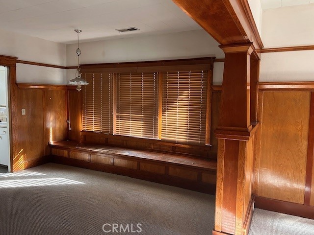 interior space featuring carpet floors, decorative columns, visible vents, and wooden walls