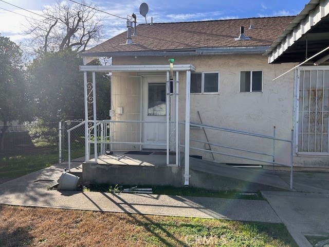 property entrance with a shingled roof and stucco siding