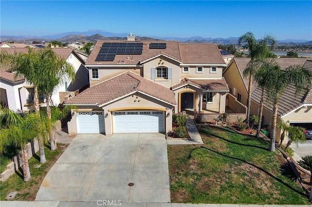 mediterranean / spanish-style house featuring a mountain view, a garage, solar panels, a tile roof, and driveway