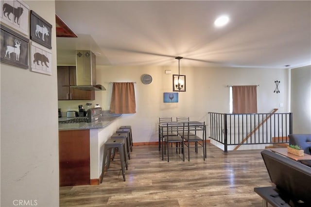 kitchen with wood finished floors, baseboards, a kitchen breakfast bar, hanging light fixtures, and island exhaust hood