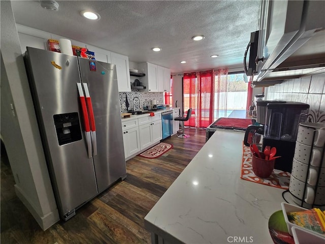 kitchen featuring stainless steel appliances, dark wood-type flooring, white cabinetry, light stone countertops, and tasteful backsplash