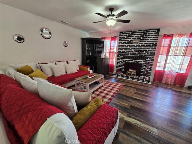 living area with dark wood-style floors, a brick fireplace, visible vents, and ceiling fan