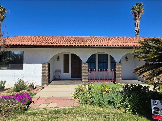 mediterranean / spanish house with a tile roof, a porch, and stucco siding