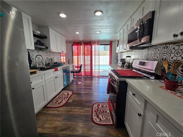 kitchen with light stone counters, dark wood-type flooring, a sink, white cabinets, and appliances with stainless steel finishes