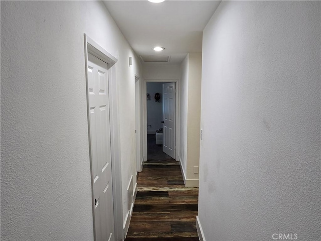 hallway featuring a textured wall, dark wood-type flooring, and baseboards