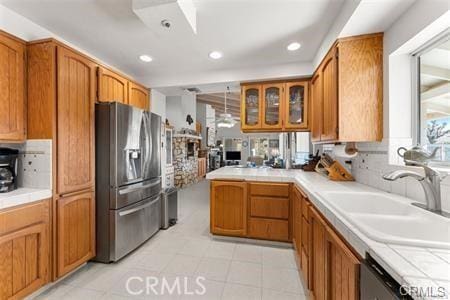 kitchen with stainless steel appliances, a sink, glass insert cabinets, and brown cabinets