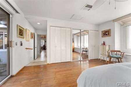 bedroom with light wood-style floors, attic access, visible vents, and two closets