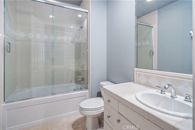 bathroom with bath / shower combo with glass door, vanity, tile patterned flooring, and toilet