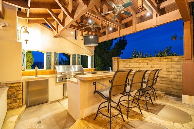 view of patio with exterior kitchen, ceiling fan, grilling area, and a bar