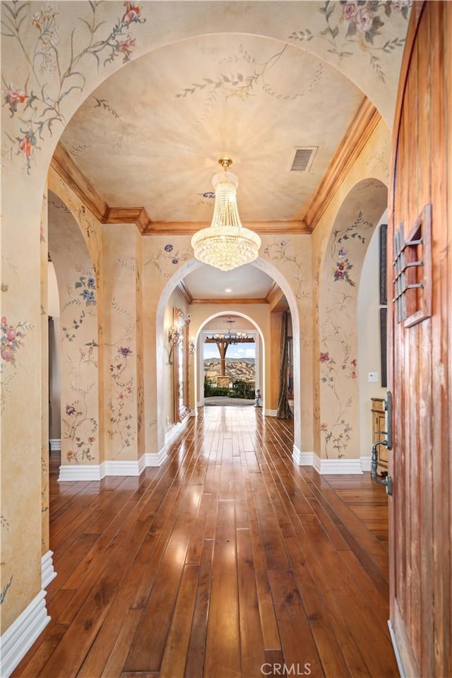 hall with arched walkways, ornamental molding, wood finished floors, and a notable chandelier