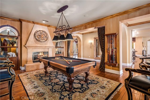 rec room featuring ornamental molding, arched walkways, a large fireplace, and wood finished floors