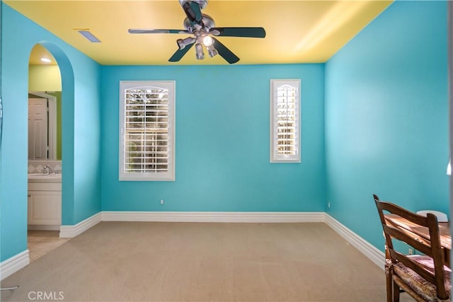 unfurnished room with arched walkways, a healthy amount of sunlight, a ceiling fan, and light colored carpet