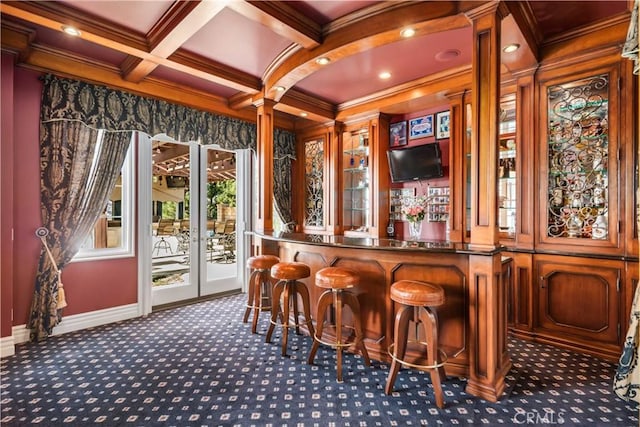 bar featuring a community bar, coffered ceiling, crown molding, ornate columns, and dark carpet