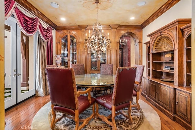 dining space with a chandelier, arched walkways, light wood-style flooring, french doors, and crown molding