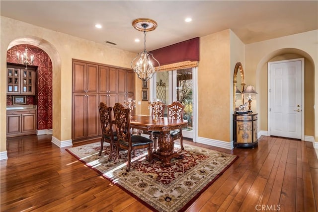 dining area with dark wood-style floors, baseboards, a chandelier, and arched walkways