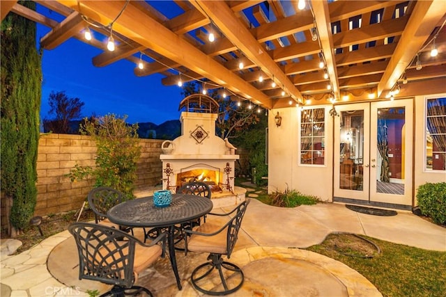 view of patio / terrace with a warm lit fireplace, fence, and outdoor dining area