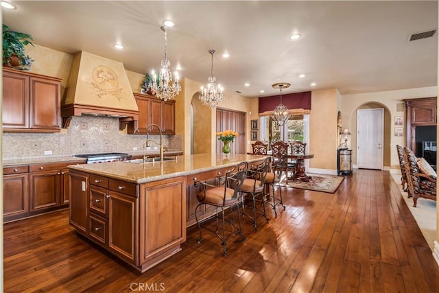 kitchen featuring arched walkways, custom range hood, visible vents, a sink, and an island with sink