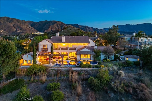 back of property at dusk with a balcony, a tile roof, a chimney, and a mountain view