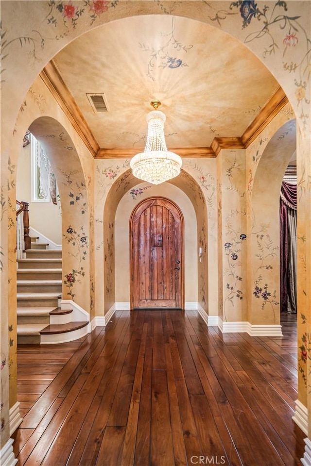 foyer with crown molding, arched walkways, dark wood finished floors, and an inviting chandelier