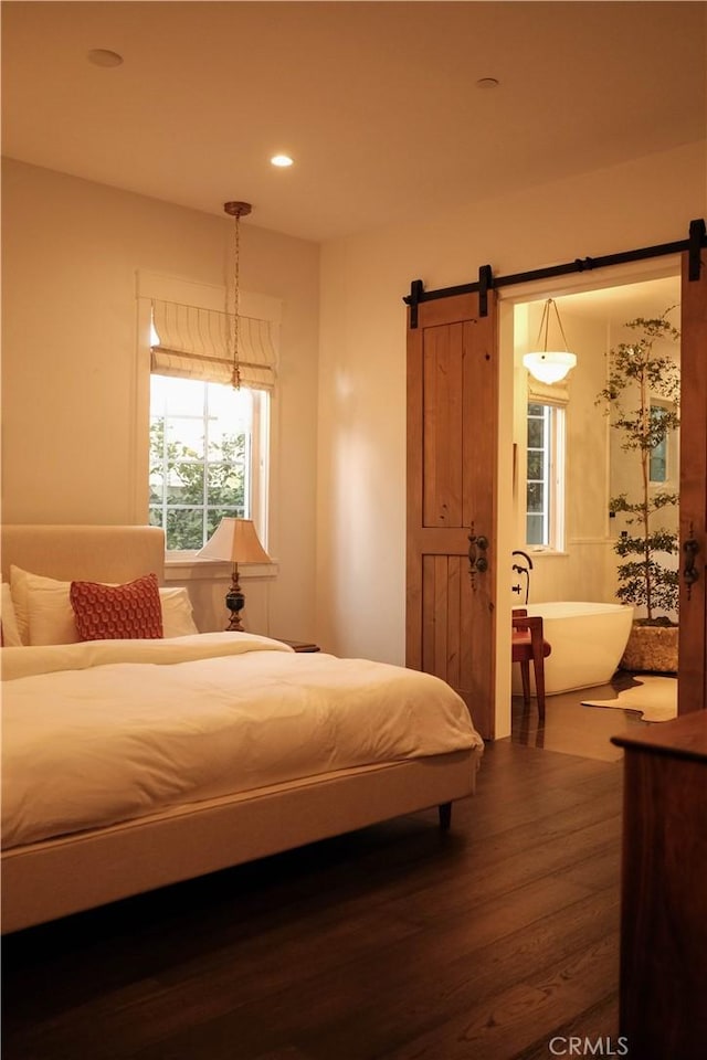 bedroom with a barn door, wood finished floors, and recessed lighting