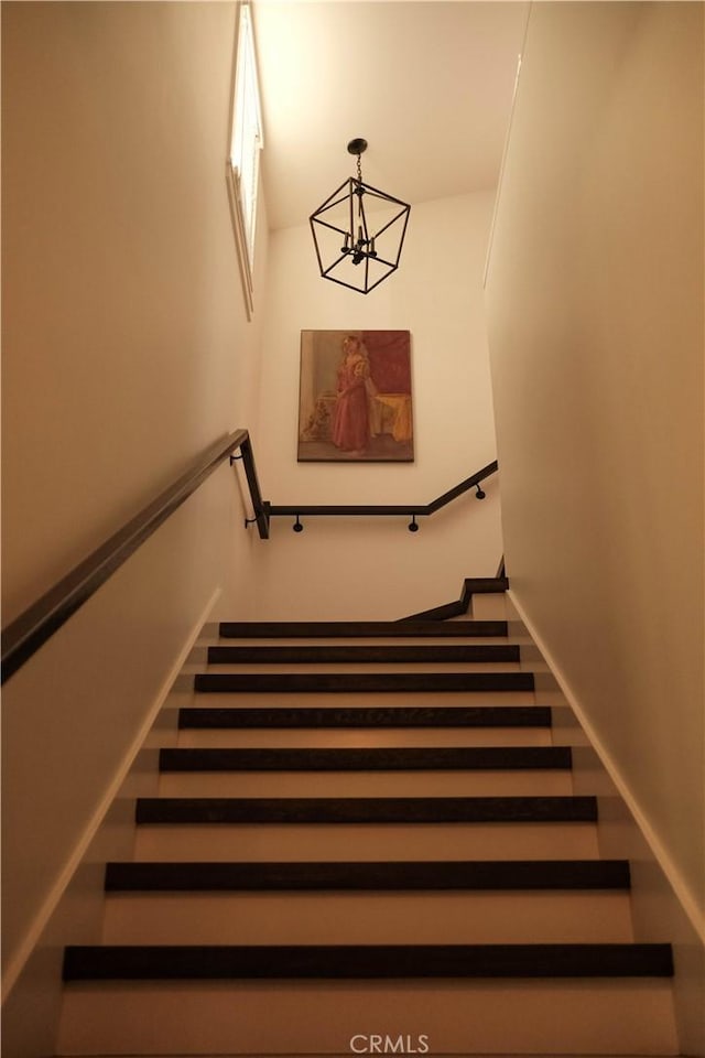 staircase featuring baseboards and a notable chandelier