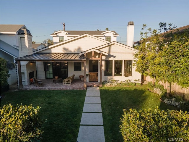 rear view of house featuring a standing seam roof, metal roof, a lawn, a chimney, and a patio area