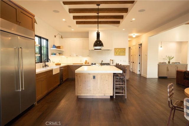 kitchen featuring a kitchen island with sink, stainless steel appliances, dark wood-type flooring, light countertops, and beam ceiling