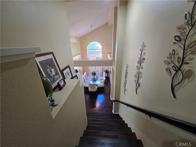 stairs featuring high vaulted ceiling, a textured wall, and wood finished floors