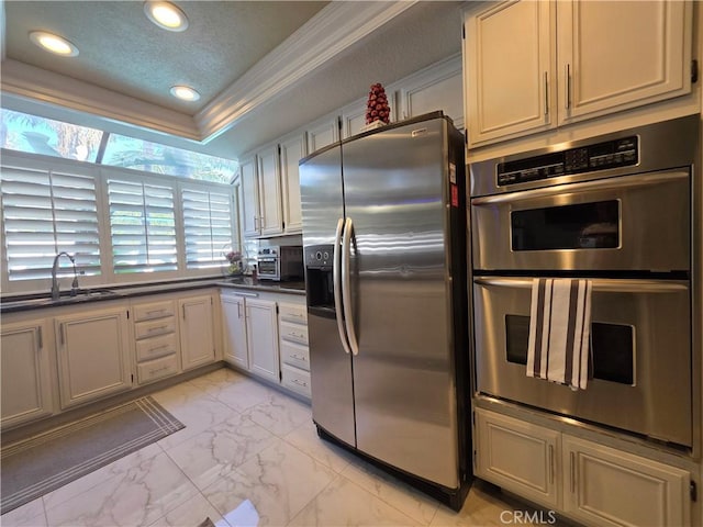 kitchen featuring white cabinets, a raised ceiling, dark countertops, marble finish floor, and stainless steel appliances