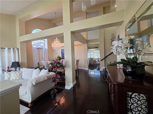 living room with dark wood-type flooring, a healthy amount of sunlight, a towering ceiling, and an inviting chandelier