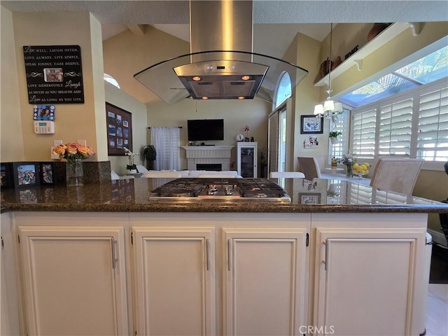 kitchen with dark stone counters, open floor plan, island exhaust hood, white cabinetry, and stainless steel gas cooktop