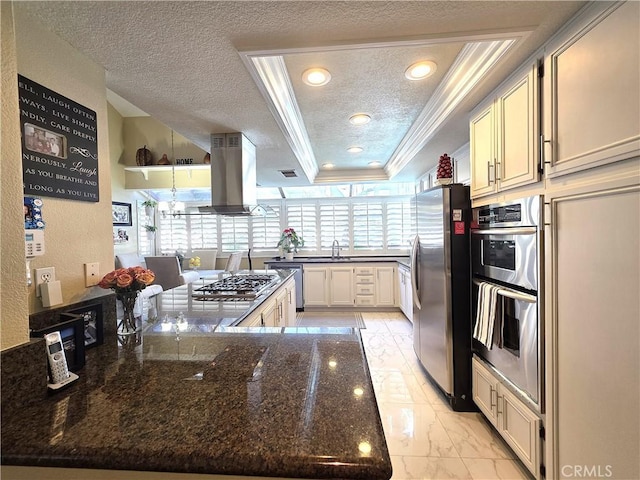 kitchen featuring island range hood, a peninsula, marble finish floor, appliances with stainless steel finishes, and a tray ceiling