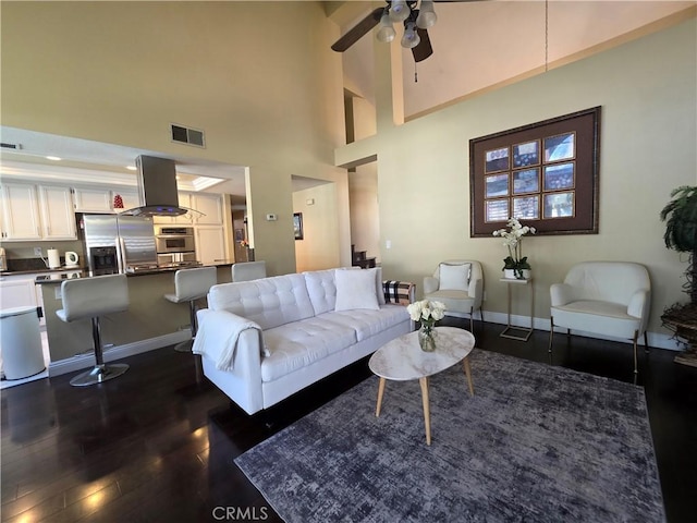 living room featuring baseboards, visible vents, a towering ceiling, ceiling fan, and dark wood-style flooring