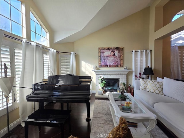 living room with high vaulted ceiling, a brick fireplace, wood finished floors, and baseboards