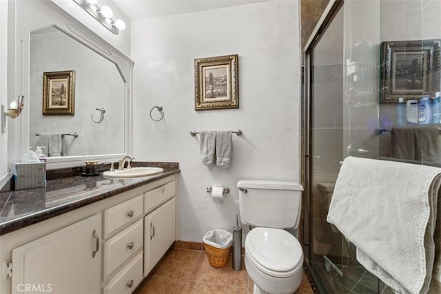 full bath with toilet, vanity, tiled shower, baseboards, and tile patterned floors