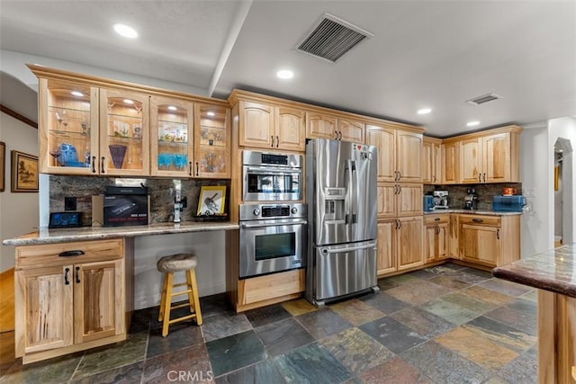 kitchen featuring stone tile flooring, visible vents, decorative backsplash, appliances with stainless steel finishes, and glass insert cabinets