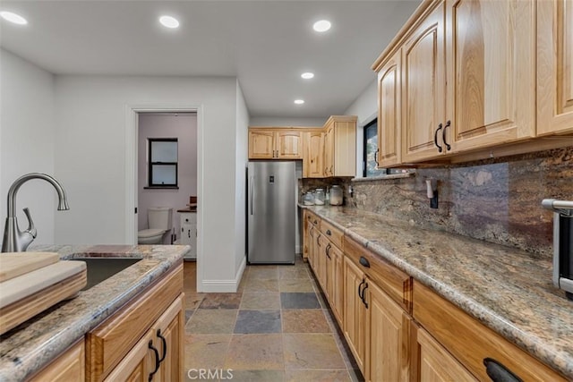 kitchen with stone tile floors, light stone counters, freestanding refrigerator, light brown cabinets, and recessed lighting