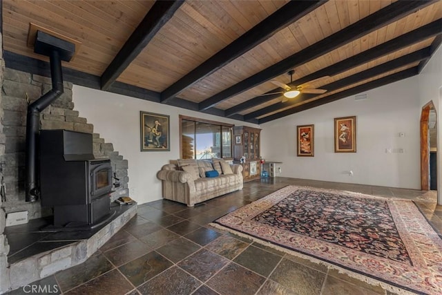 living room featuring lofted ceiling with beams, ceiling fan, wood ceiling, a wood stove, and stone tile flooring