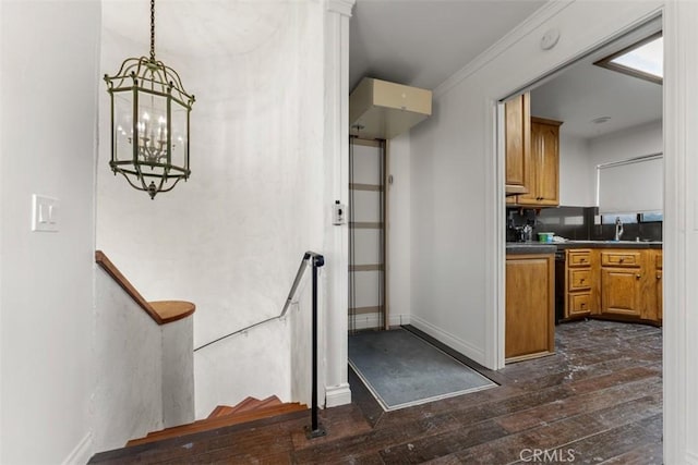 interior space featuring dark wood-style floors, brown cabinets, dark countertops, hanging light fixtures, and baseboards