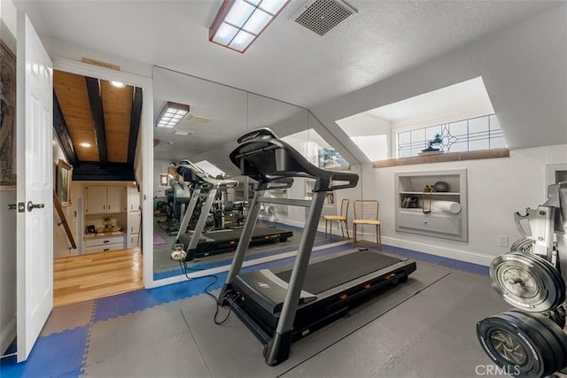 exercise area with baseboards, lofted ceiling, visible vents, and built in features