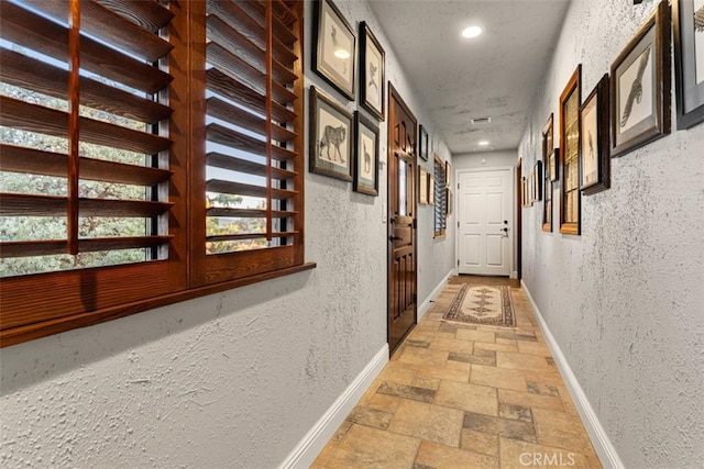 corridor with baseboards, a textured wall, recessed lighting, and stone tile floors