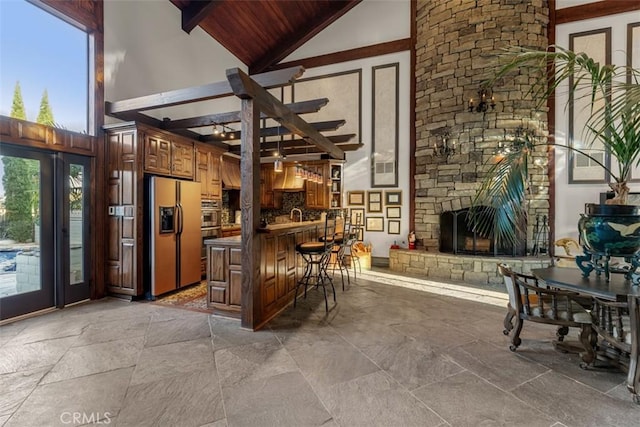 bar featuring high vaulted ceiling, fridge with ice dispenser, a fireplace, and stone tile floors