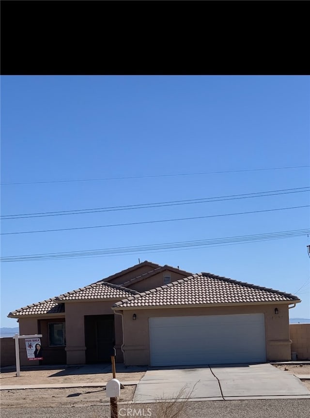 view of front of property with a garage, driveway, a tile roof, and stucco siding