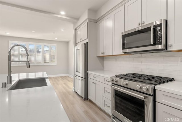 kitchen featuring light countertops, decorative backsplash, appliances with stainless steel finishes, white cabinets, and a sink