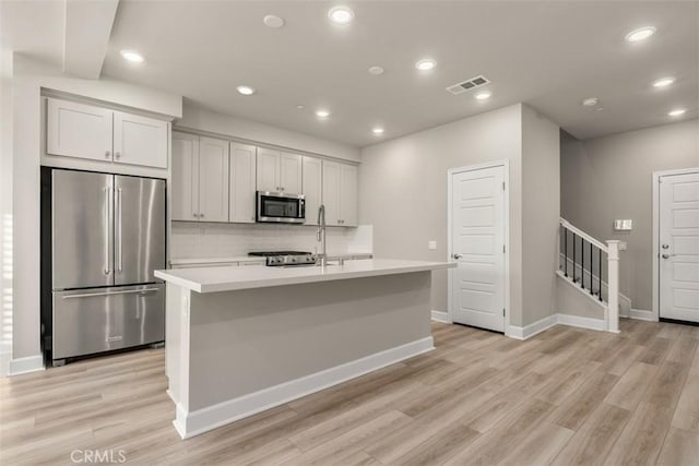 kitchen featuring stainless steel appliances, light countertops, visible vents, and an island with sink