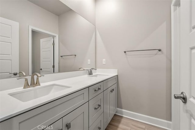 bathroom with double vanity, wood finished floors, a sink, and baseboards