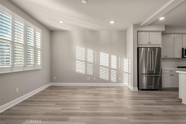 kitchen with light wood-style flooring, high end refrigerator, baseboards, light countertops, and backsplash