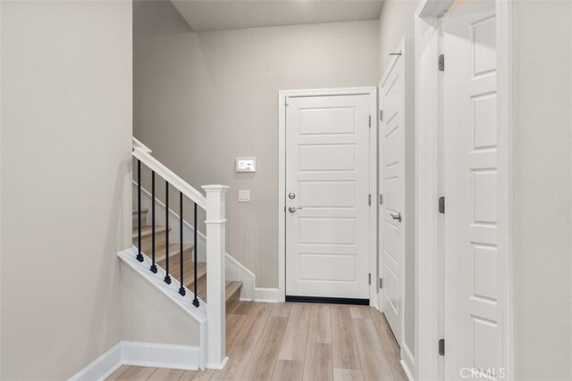 entryway with light wood-type flooring, stairs, and baseboards